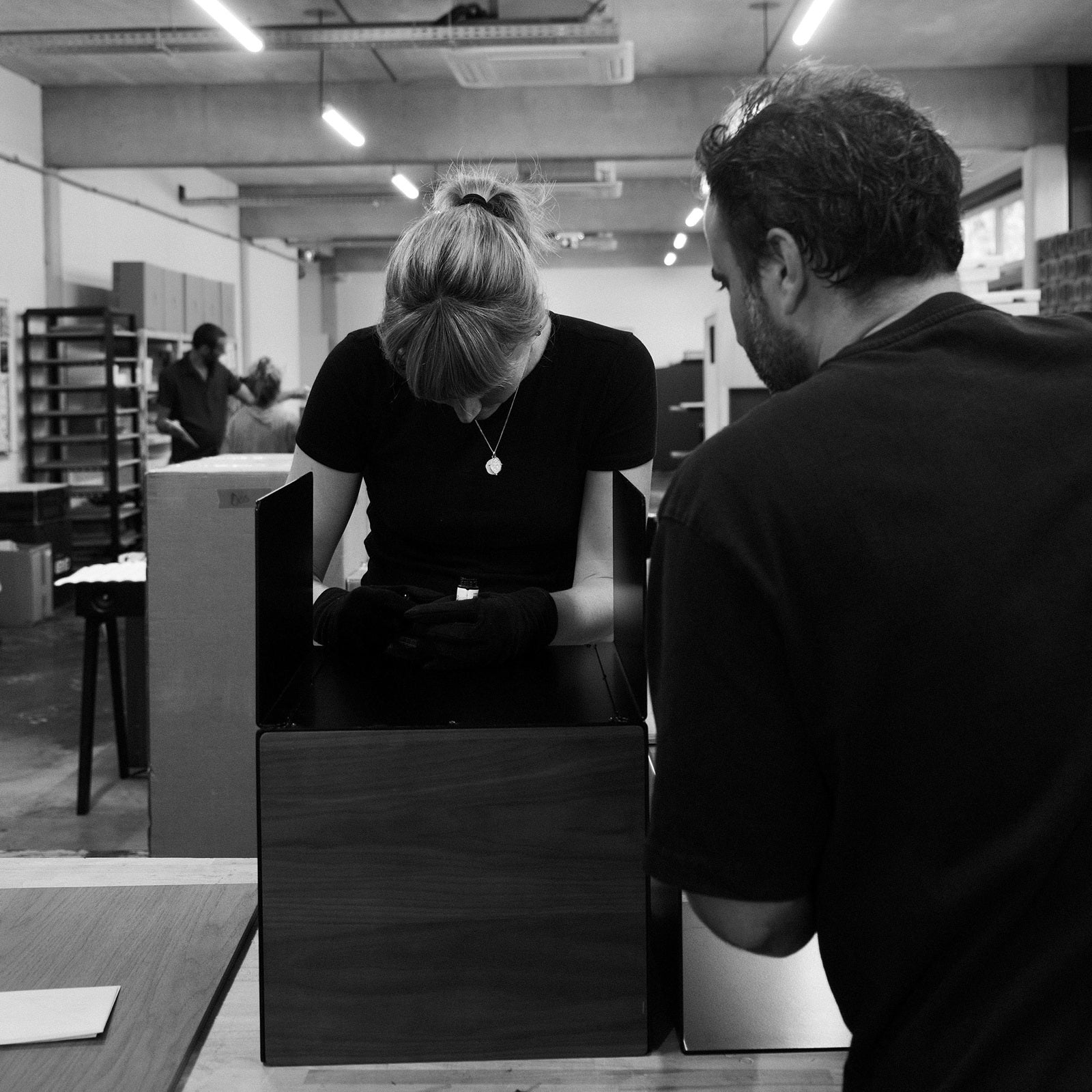 Twee meubelmakers monteren een Loia Studio platenkast van hout en staal in de werkplaats.